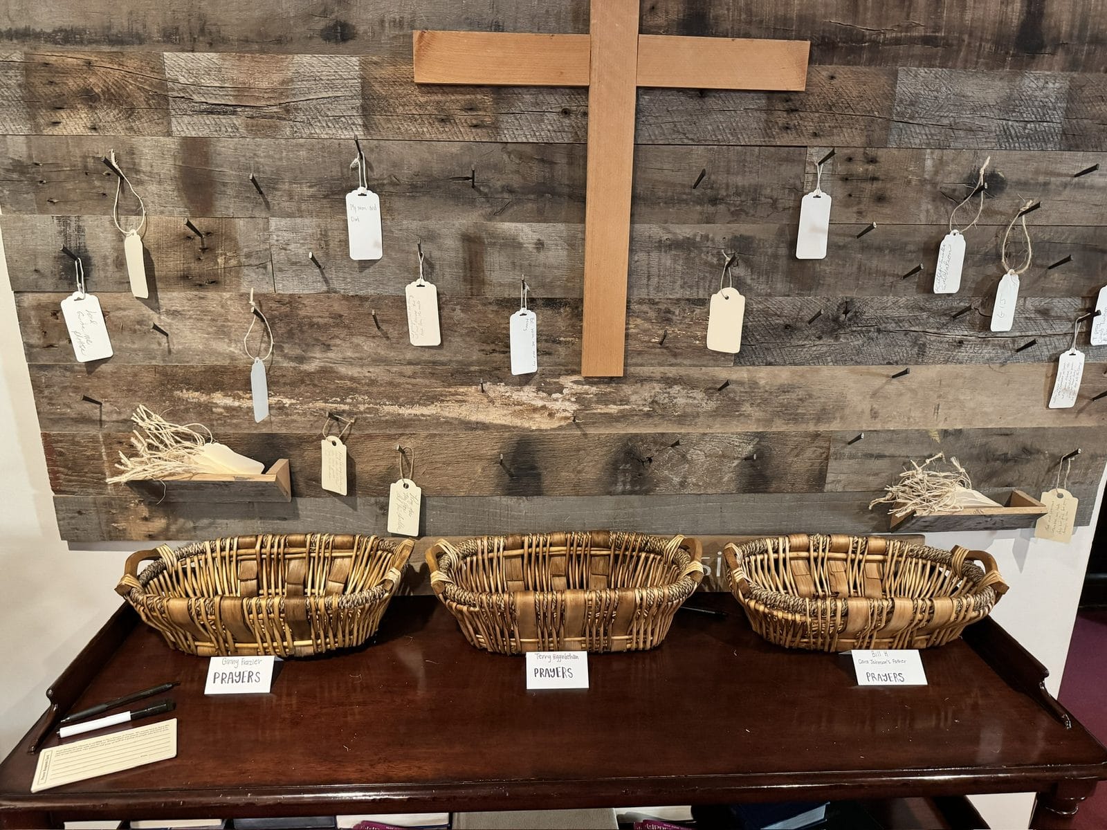 Hands resting on a wooden prayer wall covered with handwritten prayer notes